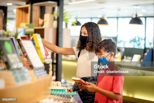 Brother And Sister Wearing Face Mask In Bookstore Stock Photo - Download Image Now - Library, Bookstore, Child