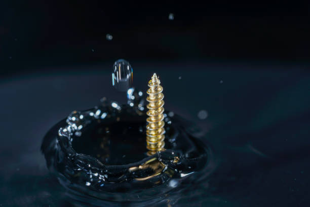 Shiny screws fall into the clear water with splashes. When immersed, air pulled along by them creates a beautiful pattern in the water.