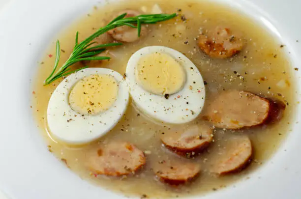 Traditional polish sour soup with sausage and eggs in a white deep plate, Eastern European meal