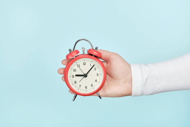 istock Red alarm clock in woman's hand on a blue background 1316295123
