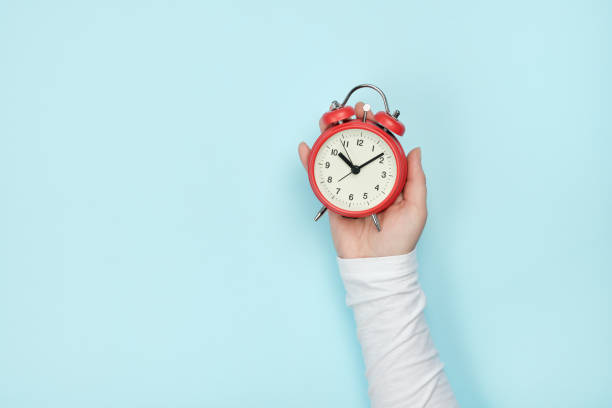 istock Red alarm clock in woman's hand on a blue background 1316295151
