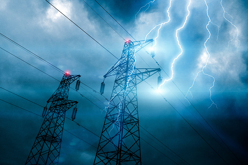 Storm lightning hitting powerline tower with bolts and plasma balls forming along electricity cables. Possible blackout. Cloudy sky with stormy weather at dusk. Digital composite.
