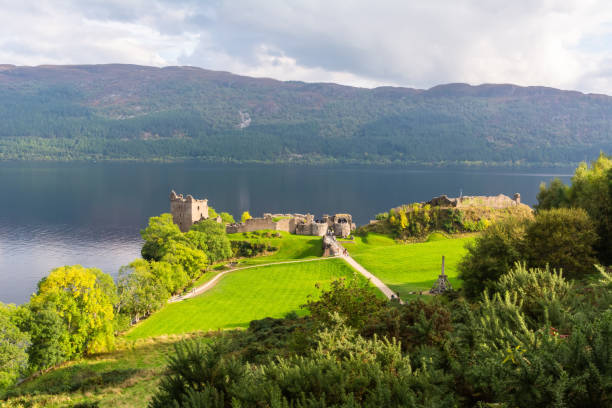 View of Loch Ness and ruined Urquhart castle in Scotland Drumnadrochit, Scotland, United Kingdom – September 25, 2017. View of Loch Ness and ruined Urquhart castle, with vegetation. The present ruins date from the 13th to the 16th centuries. drumnadrochit stock pictures, royalty-free photos & images