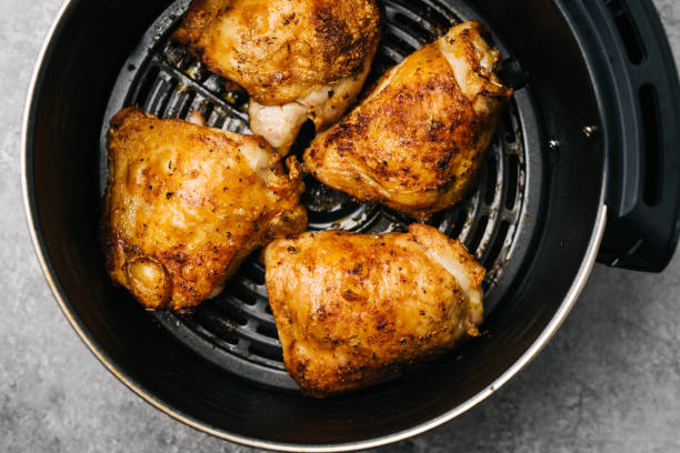 vier würzige luftgebratene hähnchenschenkel in einer luftfritteuse - chicken thighs stock-fotos und bilder