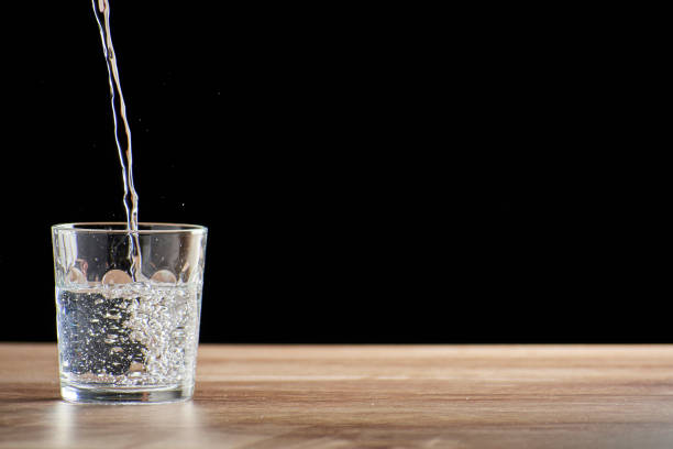 relleno de vaso de vidrio con agua sobre mesa de madera y fondo negro - barware fotografías e imágenes de stock