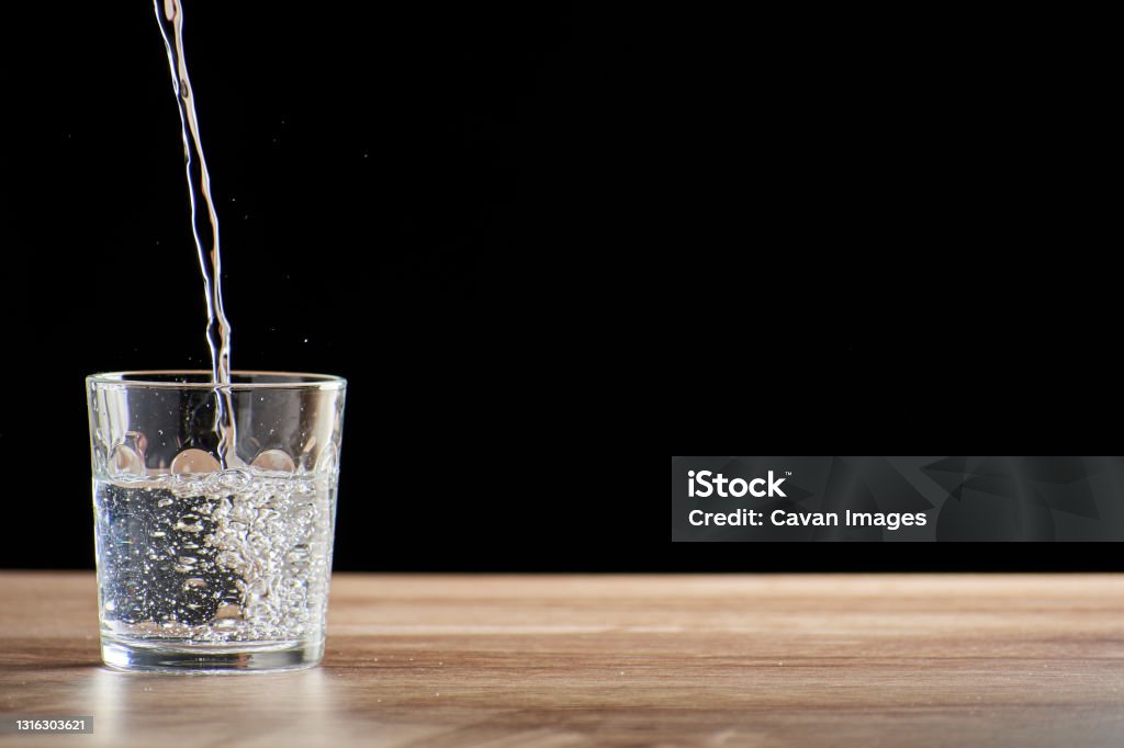 szklany kubek nadziewany wodą na drewnianym stole i czarnym tle - Zbiór zdjęć royalty-free (Ica)