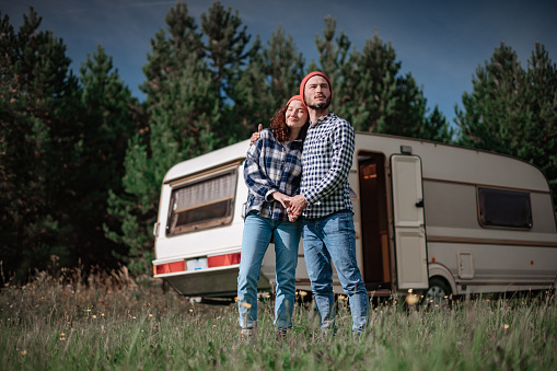 Romantic couple spending time together near trailer home. Handsome bearded man and beautiful woman enjoying company of each other. Traveling together with motor home