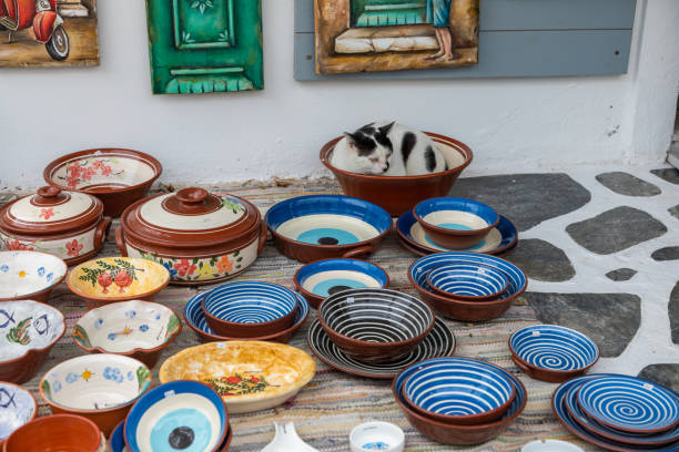 Antiparos, Cyclades, Greece - 28 September 2020: Black and white cat lying in a bowl. Local handicrafts. Gift shop.Antiparos town street on the island.