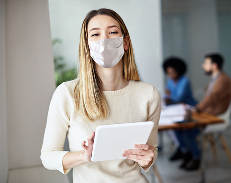 portrait of a smiling young businesswoman wearing a protective mask holding a tablet in the office