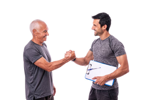 Elderly male client shaking hands in greeting to fitness trainer before training. On a white isolated background. stock photo