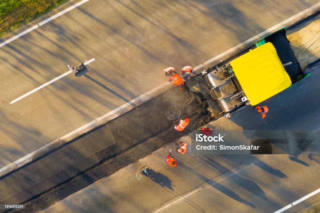 Aerial view of country road under construction Drone shot of asphalt paving machine repairing country road beside farm Road Construction Stock Photo