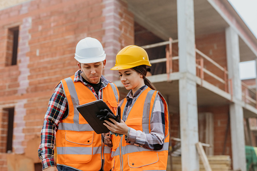 Building contractor and engineer using digital tablet while evaluating work at construction site