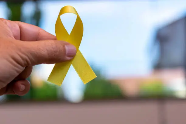 Photo of Yellow May. hand holding ribbon with yellow bow, representing accident prevention campaign.