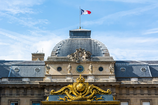 Paris, France - September 29, 2017. Architectural detail of Palais de Justice courthouse and gate with golden decoration in Paris. The courthouse houses both the Court of Appeal of Paris, the busiest appellate court in France, and France's highest court for ordinary cases, the Court of Cassation. View with statues and French flag on a sunny day.