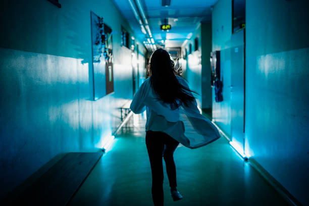 Panic female doctor rushing down a hospital corridor Rear view of female doctor rushing down the corridor of the hospital ward escaping stock pictures, royalty-free photos & images