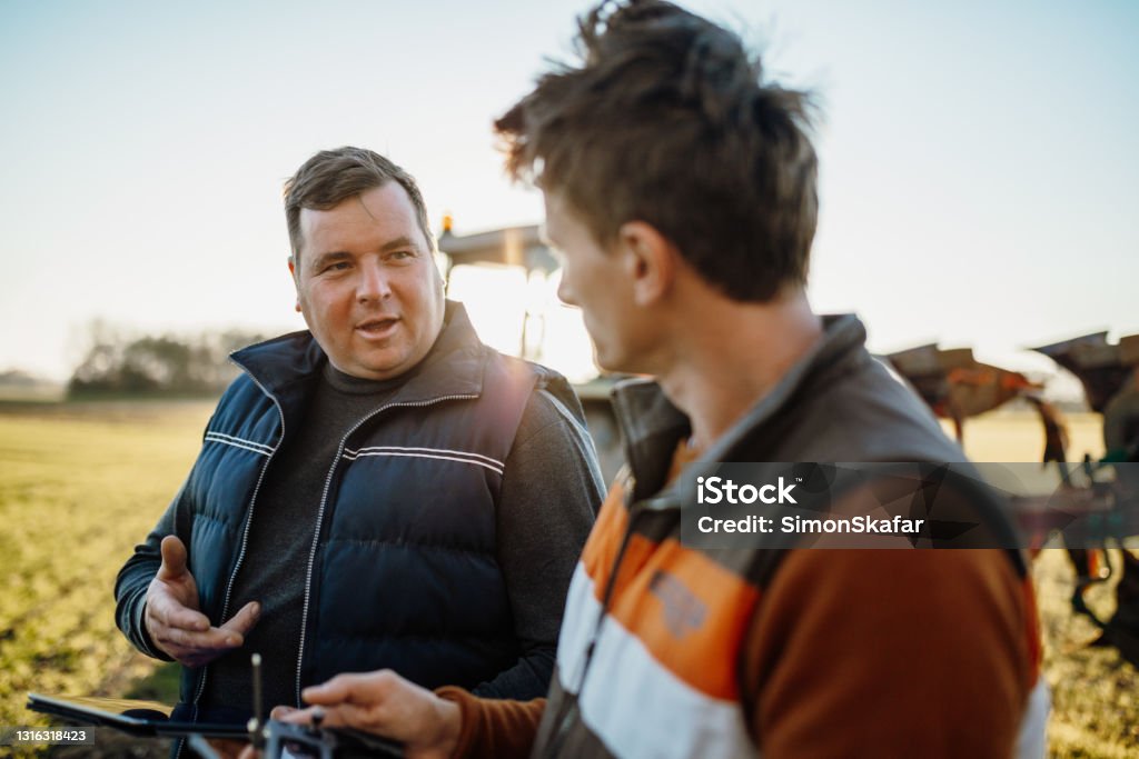 Teamwork on agricultural field Two men holding digital tablet and remote control while discussing on farm Farmer Stock Photo