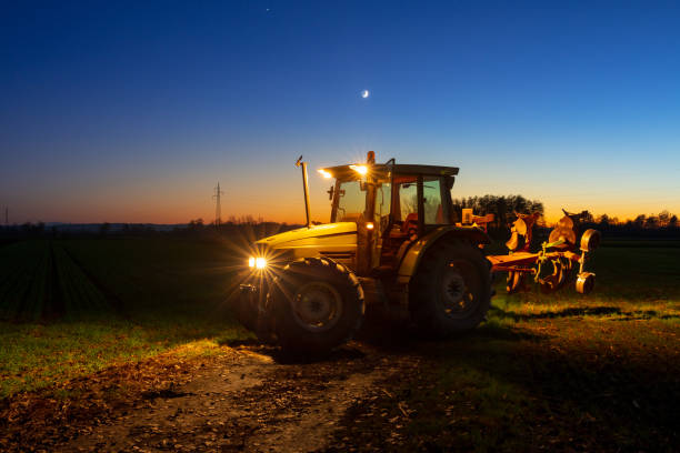 Tractor with illuminated headlight on agricultural field at night