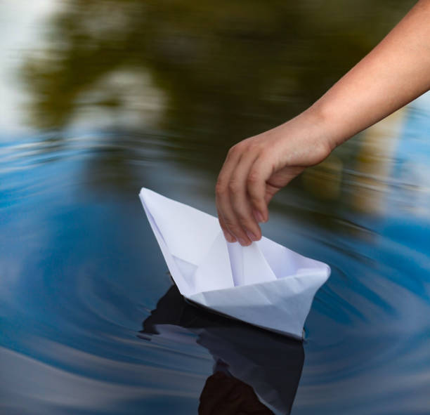 istock children hand launch paper ship in water 1316321599