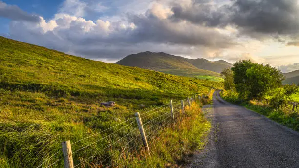 Winding country road leading toward highest mountain in Ireland, Carrauntoohil in MacGillycuddys Reeks mountains at sunset, Ring of Kerry, Coomcallee, Ireland