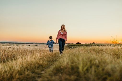 Mother and son walking on field during sunset