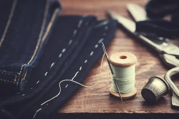 Shortening jeans. Wooden spool of  thread, thimble and scissors on table. Jeans cutting.