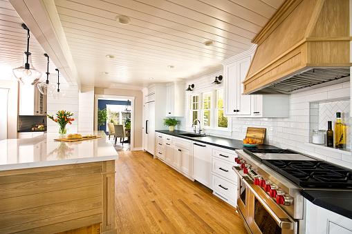 A contemporary kitchen renovation remodeling, featuring a large island, quartz counter top, hardwood floor, professional range stove and exhaust fan, kitchen sink, an open concept design to dining and living room.