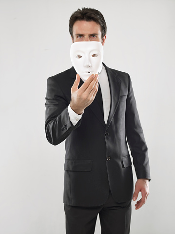 Businessman holding a masquerade mask in front of his face