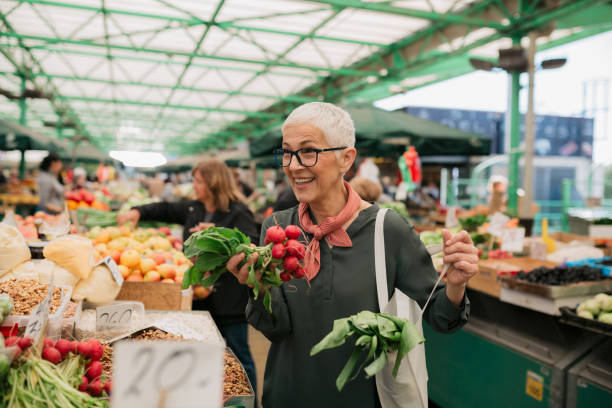 happy caucasian senior woman shopping for groceries - vegetable market imagens e fotografias de stock