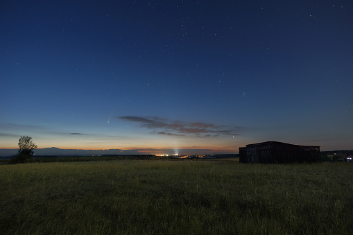 The Neowise comet in the night sky over meadow with wooden barn in morning twilight before sunrise in the Eifel, Germany