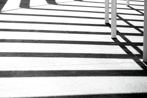 Geometric shadows on concrete path with metal pols, abstract background with copy space, full frame horizontal composition