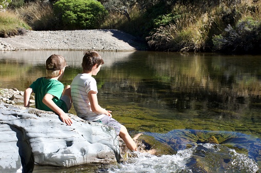 Two boys sit on a rock beside a river.  Taken in the Cobb Valley walking track in the Kahurangi National Park, near Takaka in the Tasman District of New Zealand's South Island.