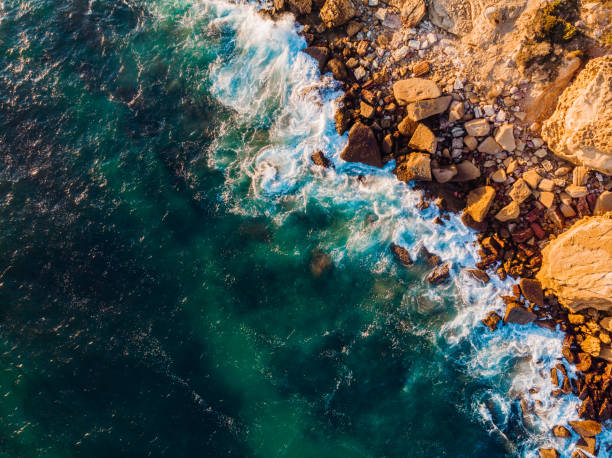 drone view of waves crashing on the rocks of the algarve cliffs, portugal, at sunset - sea foam imagens e fotografias de stock