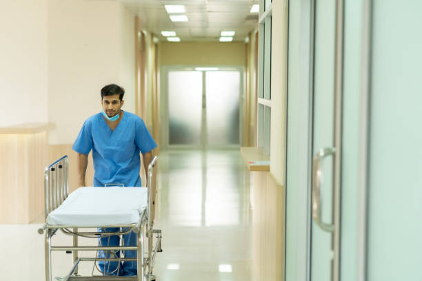 istock Caucasian male nurse in blue uniform wear improper face mask walk empty nursing bed from operating room with copyspace. 1316363204