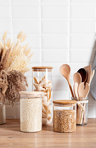 Assortment of grains, cereals and pasta in glass jars and kitchen utensils on wooden table. Healthy balanced food, sustainable lifestyle, zero waste storage, eco friendly idea