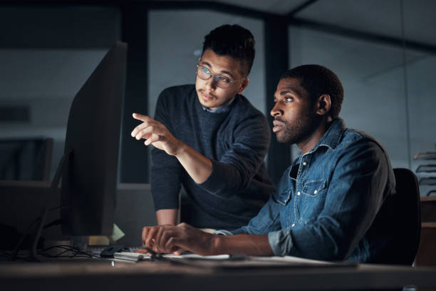 Shot of two young businessmen using a computer during a late night in a modern office