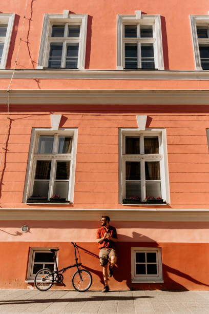 Hipster male standing with a smartphone and a city bike next to the building.
