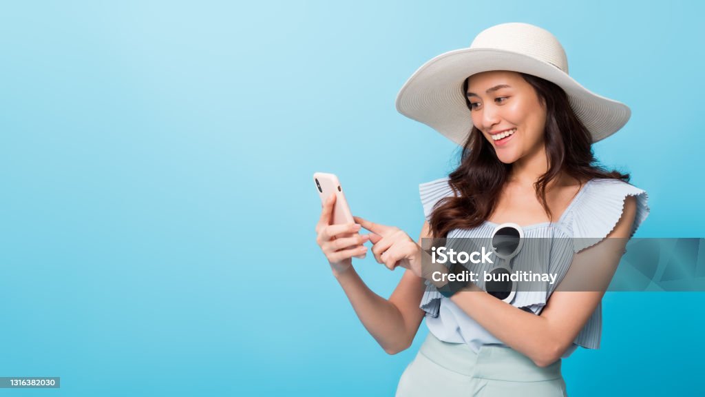 Asian pretty woman tourist preparing for travel and using smartphone isolated on blue banner background.Concept of people using technology of travel. Summer Stock Photo