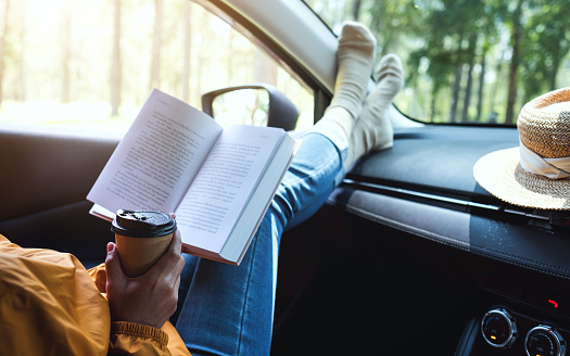 A woman reading book and drinking coffee in the car