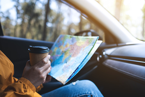 Closeup image of a woman reading a map for direction and drinking coffee in the car