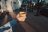 POV man holding cup with takeaway tea and lemon at the morning city