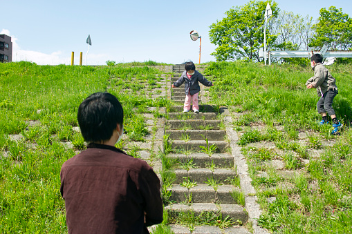 A little girl is walking down the steps. The father and elder brother is looking her carefully.