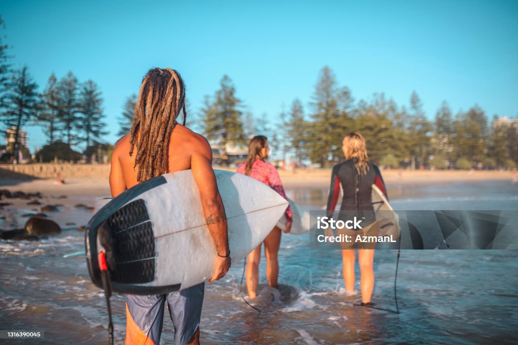 Burleigh Heads Surfers Walking in Shallow Water with Boards Rear view of male and female surfing friends in teens, 20s, and 30s walking towards shore after morning exercise. 18-19 Years Stock Photo