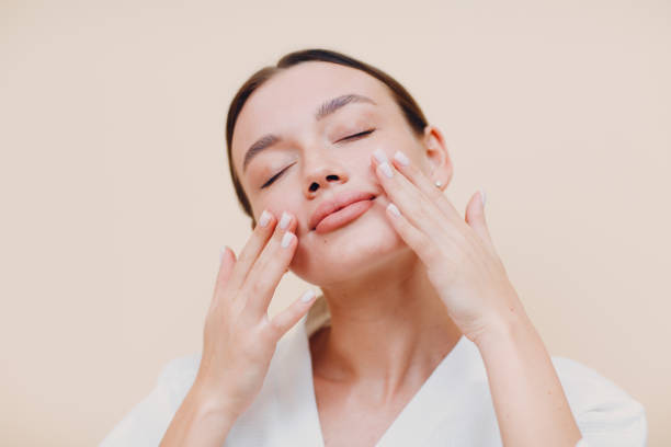 Young woman applying cosmetic white cream on her face stock photo
