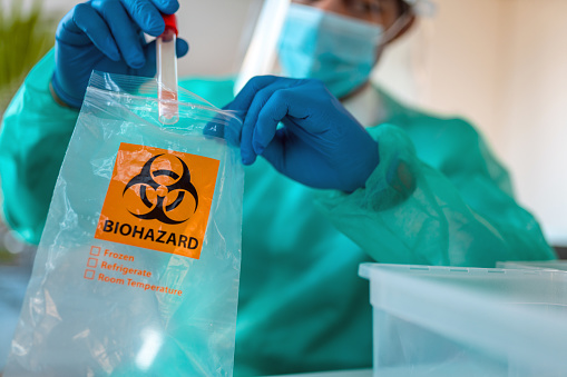 Male mixed adult doctor is putting sample in biohazard bag in doctor's office after taking nasal swab sample from patient.