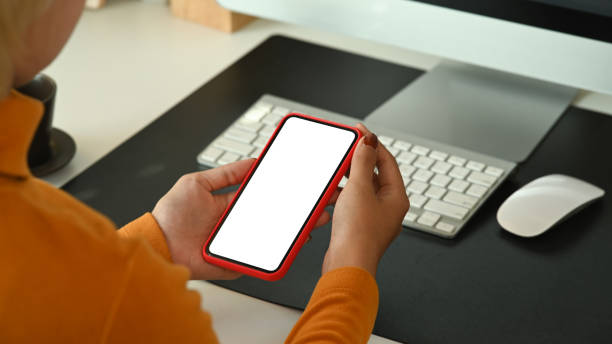 istock View over shoulder woman holding mobile phone with white screen while sitting at her office desk. 1316391102