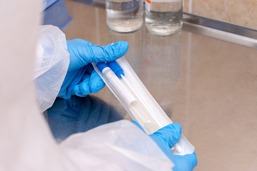 Close-up of medical worker's hands in protective clothing and gloves holding a package with a coronavirus test-tube.Medical and coronavirus concept.