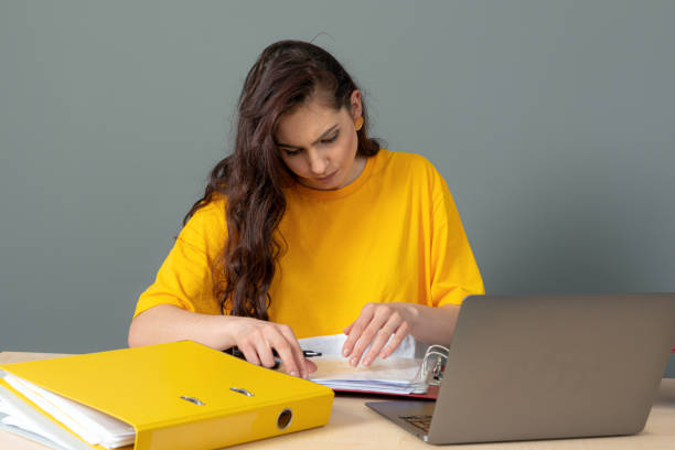 jeune femme d’affaires avec le long cheveu foncé travaillant avec le document dans le bureau, isolé sur le fond gris - paper document pen long hair photos et images de collection