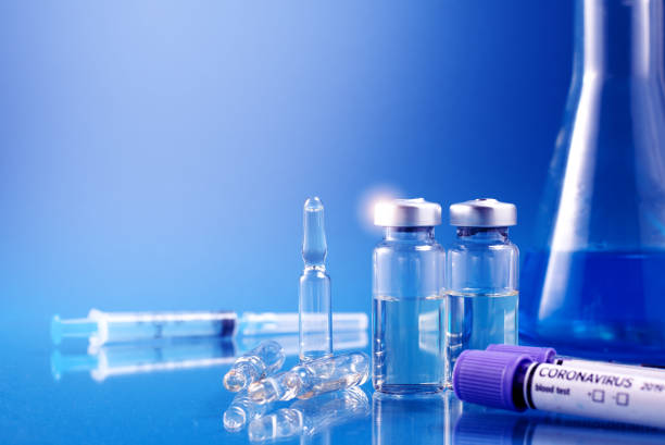 istock Glass ampoules with liquid for injection against laboratory flasks on dark background. Vaccination from coronavirus Covid-19 theme 1316397386