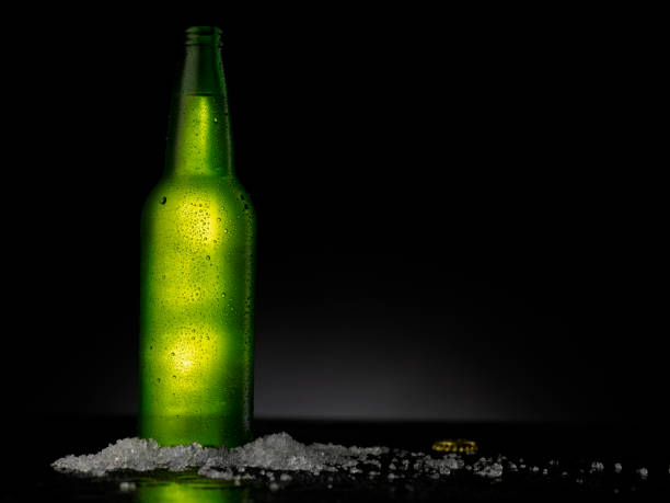 istock Ice Cold Green Beer Bottle Covered with water drops - condensation. Blank for drink beverage product design mock-up.  Standing on black table with dark - black background. 1316397592