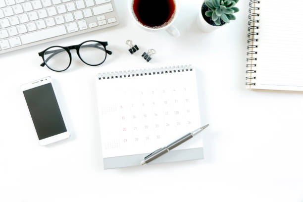 istock Modern white office desk table with computer, calendar, notebook, tree, glasses and cup of coffee. Top view with copy space, 1316397760
